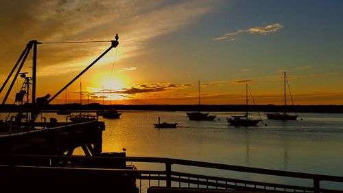 Silhouette boats moored at harbor against sky during sunset