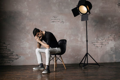 Portrait of young man sitting on chair by wall