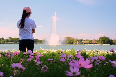 Woman standing by flowering plants against sky