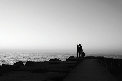 Rear view of people standing on beach against clear sky