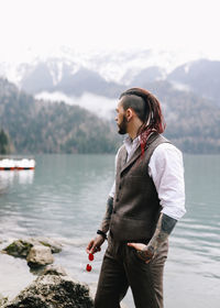 A man a groom a hipster with dreadlocks in a wedding suit stands by sea and mountains in nature