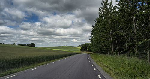 Empty road amidst field against sky