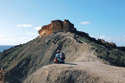 Rear view of woman sitting on cliff against sky