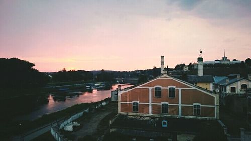 Buildings by river against sky at sunset