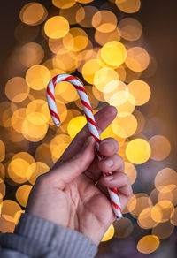 Close up of hand holding candy cane with light bokeh in background.