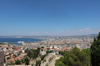 Aerial view of townscape by sea against blue sky