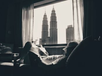 Man lying on sofa with view of petronas towers seen through window