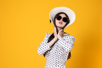 Young woman wearing sunglasses standing against yellow background