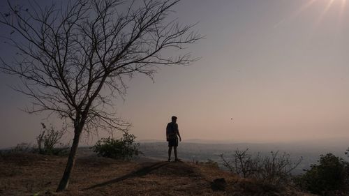 Silhouette man standing by tree against sky during sunset