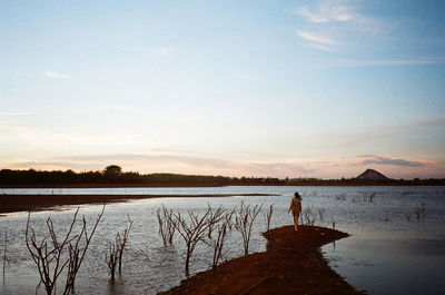 Silhouette man standing by lake against sky