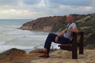 Rear view of man siting at beach against sky