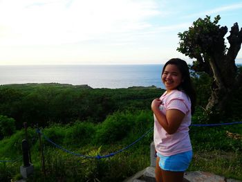 Portrait of smiling girl standing on tree by sea against sky