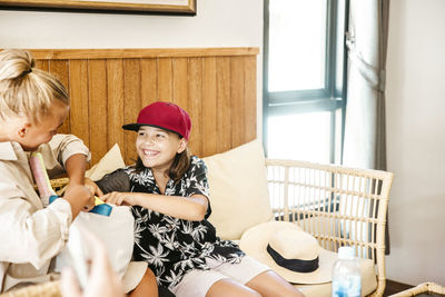 Happy daughter talking with mother holding bag while sitting in hotel room during vacation