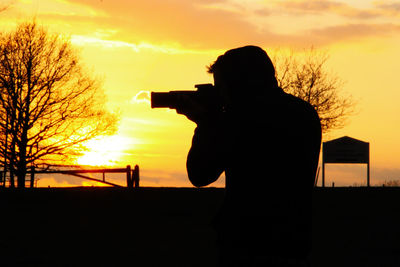 Silhouette man photographing at sunset