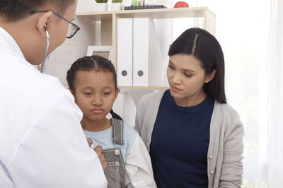 Mother looking at doctor examining girl in clinic