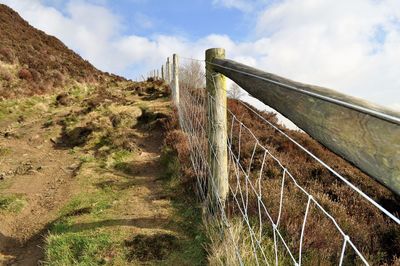 Fence on mountain against cloudy sky