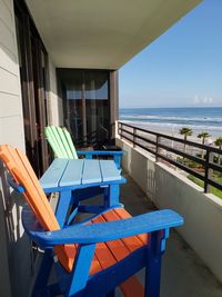 Empty chairs and tables by sea against sky