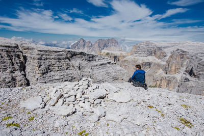 Man sitting on rock by mountains against sky