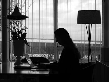 Side view of silhouette woman using laptop while sitting on table at home