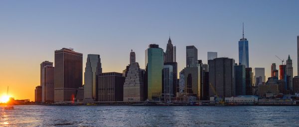 East river against modern buildings at manhattan during sunset