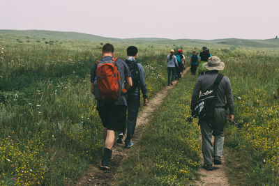 Rear view of people walking on field against sky