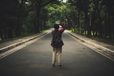 Rear view of woman standing on road amidst trees