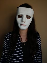 Close-up portrait of young woman wearing mask against wall