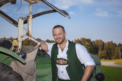 Portrait of smiling man in traditional clothing standing by old vehicle against sky