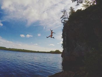 Low angle view of woman jumping into river from cliff against sky