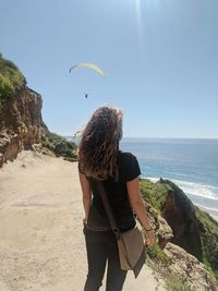 Rear view of woman standing on rock by sea against sky