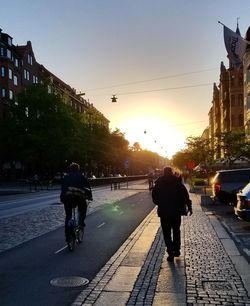 People riding bicycle on road against sky during sunset