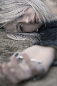 Close-up of thoughtful young woman holding key pendant while lying on sand