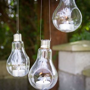 Lit candles inside hanging light bulbs outdoors