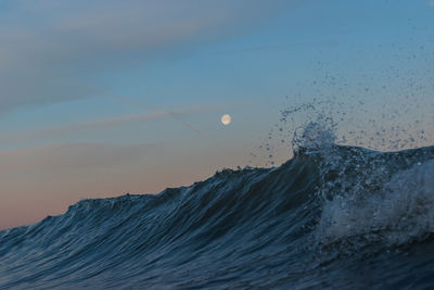 Sea waves splashing against sky at full moon