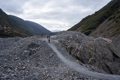 Trail leading towards mountains against cloudy sky