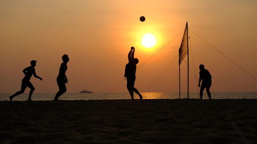 Silhouette people playing on volleyball at beach against sky during sunset