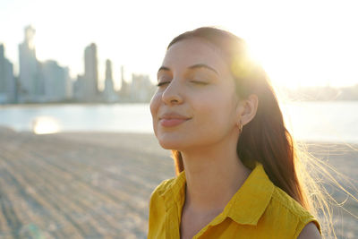 Portrait of girl on sand beach breathing fresh air at sunset with city skyline on the background