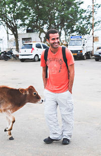 Smiling young man with backpack looking away while standing by calf on road