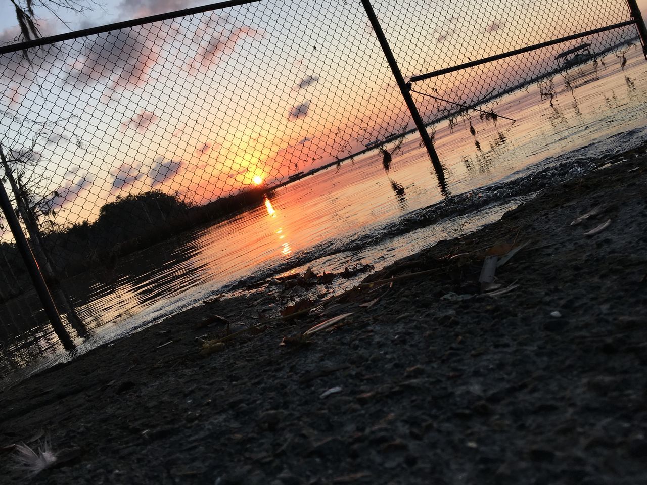 sunset, water, wet, sunlight, sun, transportation, reflection, street, no people, orange color, sky, built structure, glass - material, sunbeam, outdoors, chainlink fence, window, rain, architecture, nature