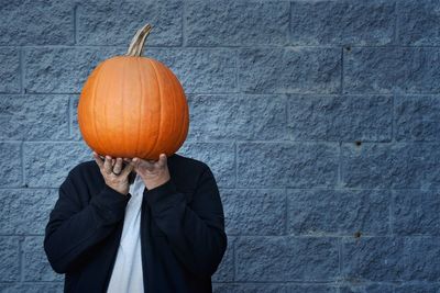 Person holding pumpkin against wall