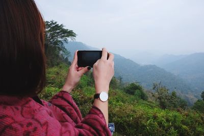 Woman photographing through mobile phone against sky