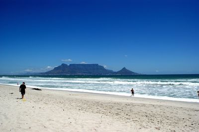 People on beach against clear blue sky