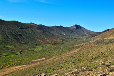 Scenic view of land and mountains against blue sky