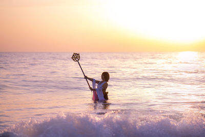 Young woman holding wand in sea during sunset