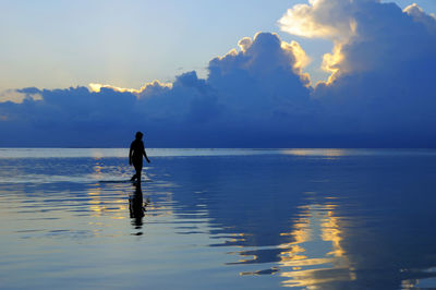 Rear view of woman standing in sea against sky during sunset