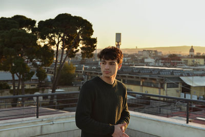 Portrait of young man standing on railing against cityscape