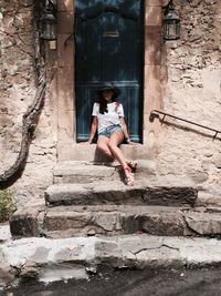 Full length of woman sitting against house