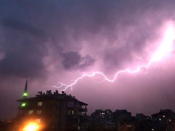 Lightning over illuminated building against sky at night