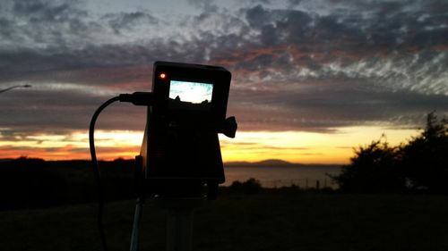 Close-up of camera phone against sunset sky