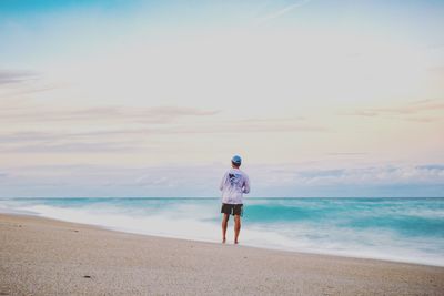 Rear view of man standing on beach against sky